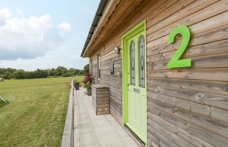 A wooden cabin with a lime green door and number 2 on the wall beside a grass field at Lulu Logs in Congresbury