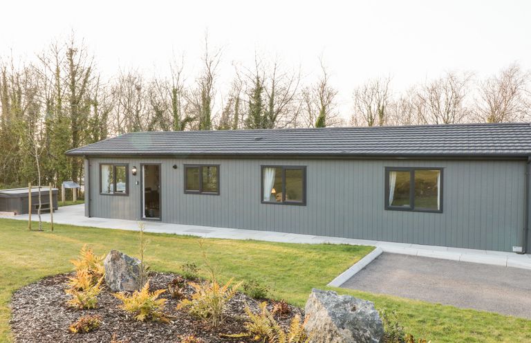 A single story gray house with black roof windows and a garden bed with rocks and plants at Mayflower in Broadwoodwidger near Ashwater