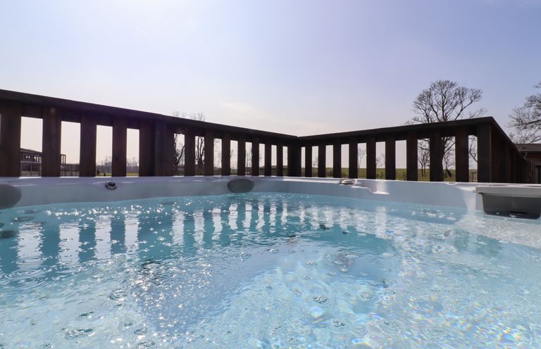 An outdoor jacuzzi with bubbling water and wooden railing around at Skylarks in Fornham St Genevieve near Bury St Edmunds