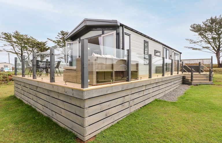 A raised wooden deck with glass railing around a modular home with outdoor furniture on the deck at Puffin Lodge in Broad Haven