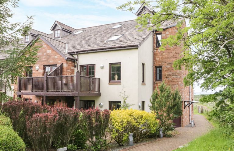 A residential building with a balcony surrounded by bushes and trees at Cosy Corner in the Lakes Greystoke