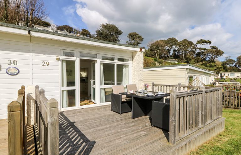 A wooden deck with a table and chairs outside a white cabin with large windows at Seas The Day in Ventnor