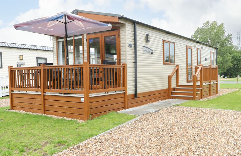 A mobile home with a wooden deck, outdoor table and umbrella at Audrey's Lodge Foxburrow Hang in Fritton