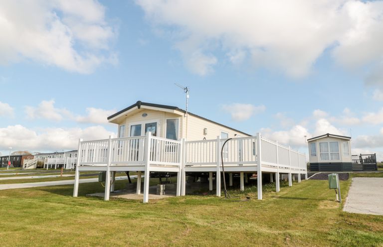 A mobile home with a white railing deck on a grassy plot at Moonlight Lodge in Bockenfield Country Holiday Park near West Thirston