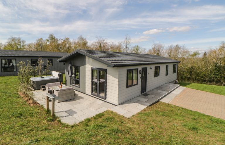 A single story house with an outdoor seating area and hot tub in a grassy yard at Meadow Lodge in Lifton