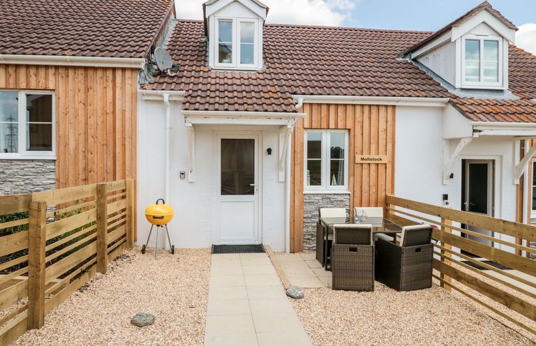 A patio area with a yellow barbecue grill a dining table with chairs and a wooden fence at Mellstock in Nottington near Weymouth