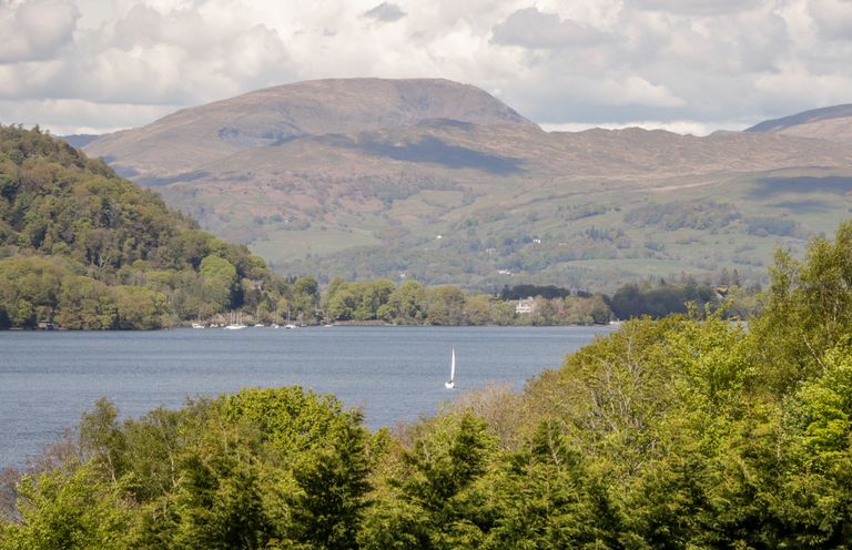 A lake with a sailboat surrounded by trees and hills at Howgill Lodge in Gatebeck near Kirkby Lonsdale