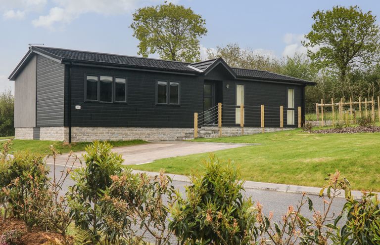 A black single-story house with a stone foundation near a paved driveway and green lawn at Lily Broadwoodwidger near Ashwater