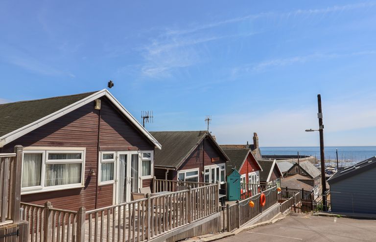 A row of wooden cabins with railings and a view of the sea at Granny's Teeth in Lyme Regis