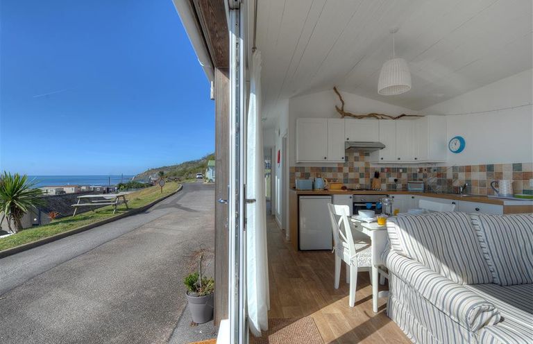 A kitchen and dining area with white cabinets and striped sofa at The Beach Hut in Lyme Regis