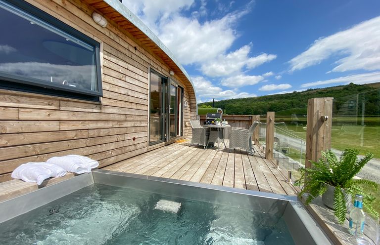 An outdoor wooden deck with a hot tub towels and table with chairs overlooking a grassy landscape at Low Longlands in Cartmel