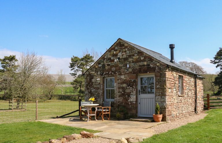 A stone cottage with a table and two chairs outside on a paved area at Herdie Hideaway in Appleby-In-Westmorland