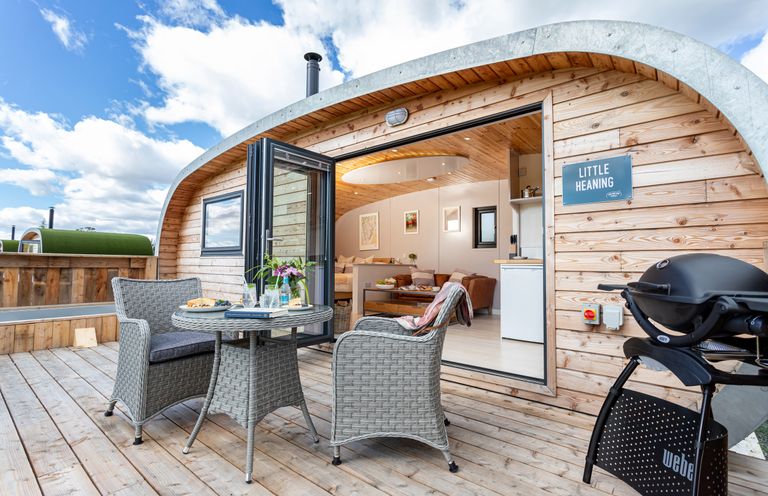 A wooden patio with table and chairs next to an open door to a living area at Little Heaning in Cartmel