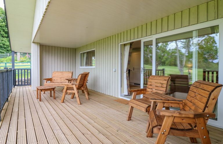 A covered patio with wooden chairs and tables overlooking a grassy area at The Lodge in Blairgowrie
