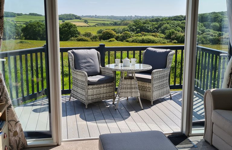 A balcony with two chairs and a table with cups and teapot overlooking green fields at Vendee Lodge Thorness Bay Holiday Park near Cowes