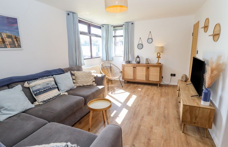 A living room with a grey sofa a wooden TV stand and cabinet and a round side table at Rollin Dunes in Humberston Lincolnshire