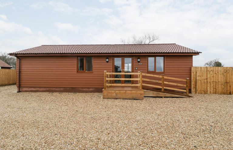 A brown lodge with a tiled roof two windows and a wooden ramp and railing at Bluebell Lodge Meadow view lodges in Brean