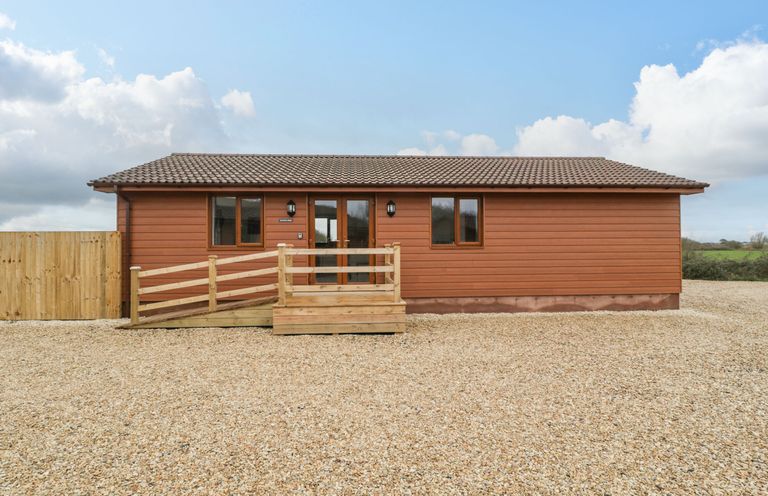 A single story wooden lodge with a ramp and gravel driveway at Delphine Lodge Meadow View Lodges in Brean
