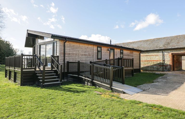 A wooden lodge with a deck and ramp on a grassy area at Manor Farm Lodge in Bowerchalke