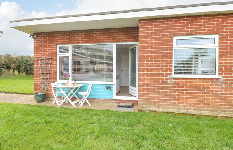Exterior of a brick building with a small white table and two chairs on a patio at 12 Siesta Mar in Mundesley