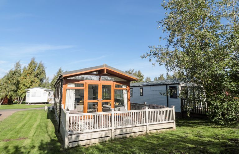 A mobile home with wooden framed glass doors and a fenced porch on a grassy plot at Pinecone Lodge No 9 Felmoor Park near Felton