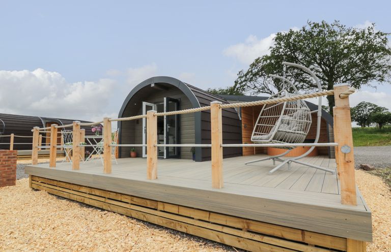 An outdoor deck area with a hanging chair and a small table with chairs in front of a pod-style building at Laird Lodge 1 in Lochmaben