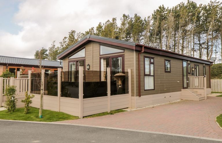 A modern single-story cabin with a fenced patio and paved driveway surrounded by trees at Rockpool Retreat in Runswick Bay near Hinderwell