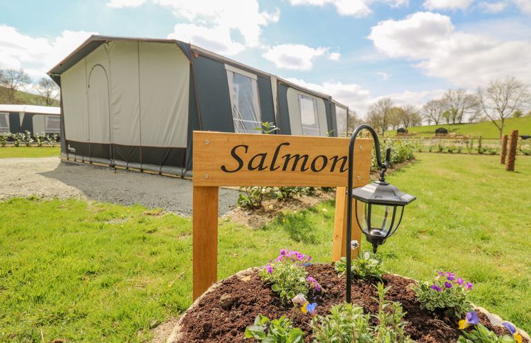 A camping tent with a wooden sign saying Salmon and a flower bed with a lamp at The Salmon in Nantmel near Rhayader