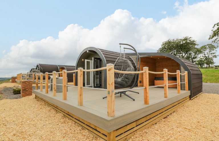 A wooden pod structure with a deck railing and hanging chair outdoors at Laird Lodge 2 in Lochmaben