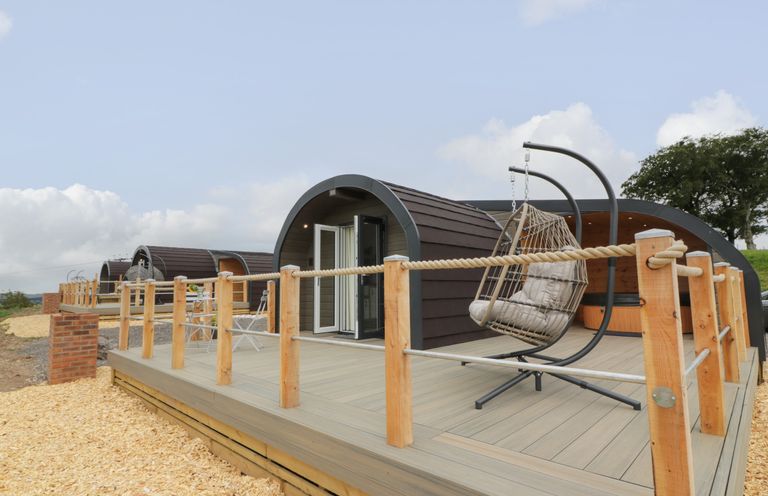 A wooden deck with hanging chair and seating area outside curved small cabins at Laird Lodge 3 in Lochmaben