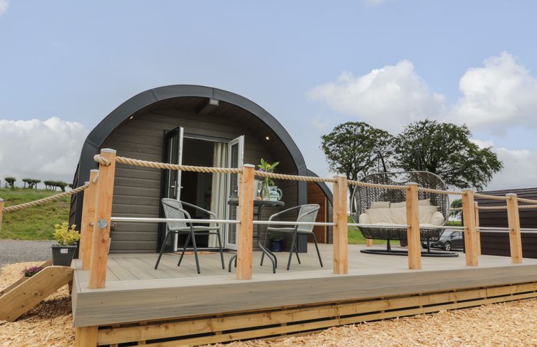 A wooden pod with an outdoor deck with two chairs a round table and a hanging chair at Laird Lodge 4 in Lochmaben