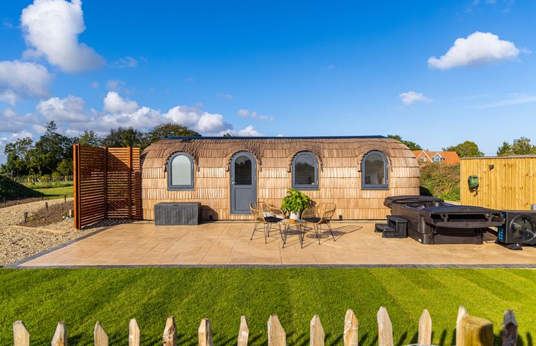 A small building with rounded roof and four arched windows and door a table with two chairs and a hot tub on a patio at Indrek - Mayflower Meadow in Brandesburton