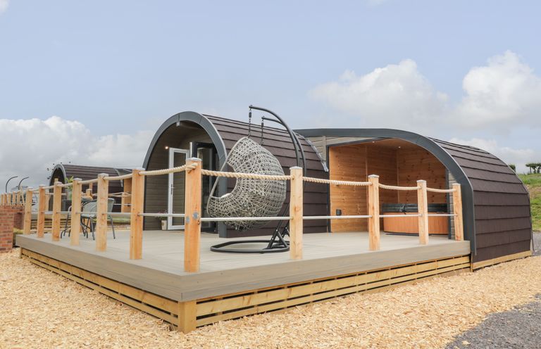 An outdoor deck with a hanging chair and seating area in front of curved wooden pods at Laird Lodge 5 in Lochmaben