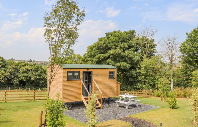 A wooden cabin on wheels with a picnic table outside in a grassy area with trees at Rose in Illogan