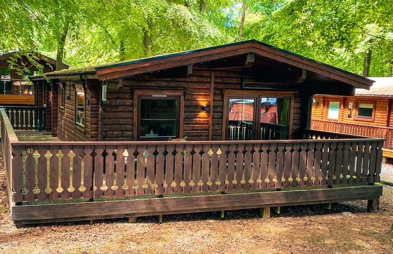 A wooden cabin with a covered porch and railing surrounded by trees at Leafy Hollow Lodge in Louth