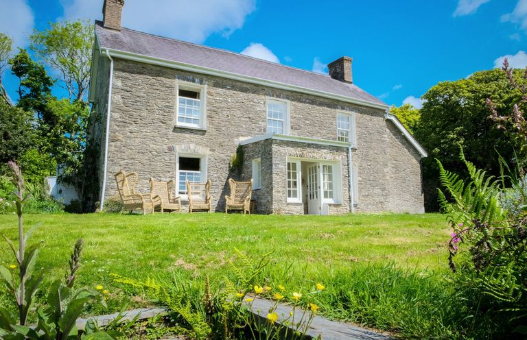 Stone house with lawn and outdoor wicker chairs at Henllys Newport Pembrokeshire