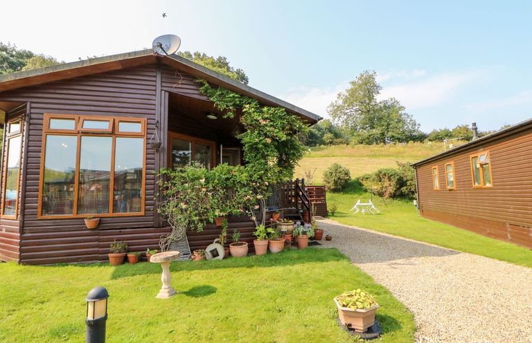 A wooden cabin with potted plants and a gravel pathway on a grassy lawn at 6 Badgers Retreat Tunstall near Richmond