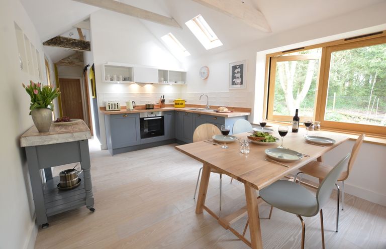 A kitchen with a wooden dining table set for four and gray cabinets under skylights at Red Poll Barn Spexhall Near Halesworth