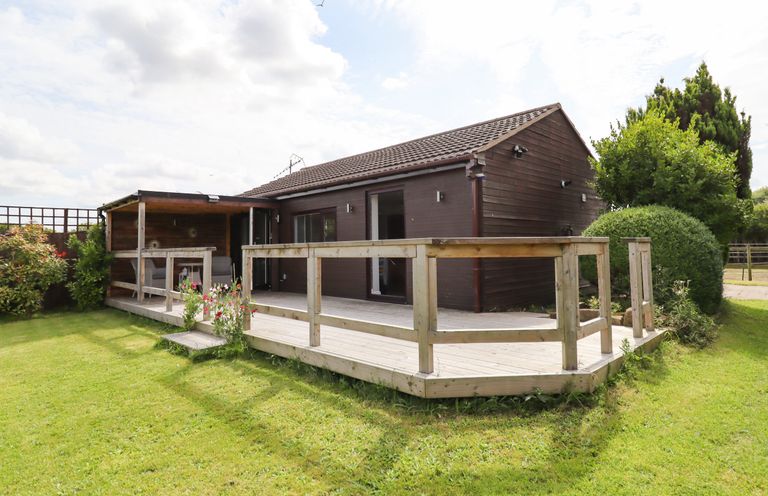 A wooden cabin with a deck and garden surrounding it at Meols Holiday Lodge in Meols