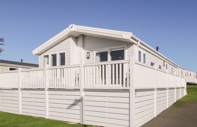 A white mobile home with a white fenced deck on a grassy area at Dershel Lodge in Southerness