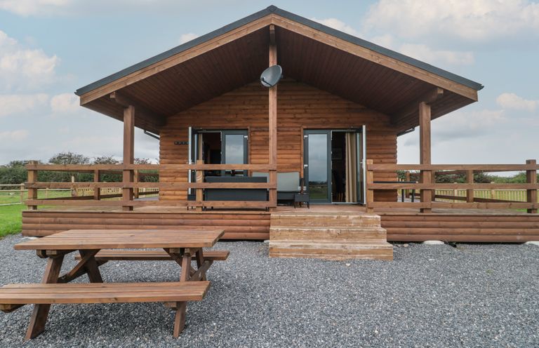 A wooden cabin with a small porch and picnic table in front at The Lodge at Crossroads Farm in Middlezoy