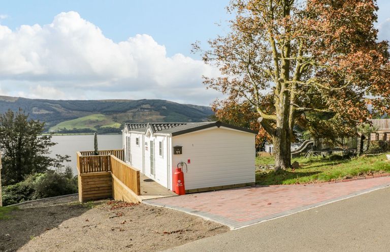 A small white cabin next to a large tree overlooking a body of water and hills at 11 Mansion View in Helensburgh near Kilcreggan