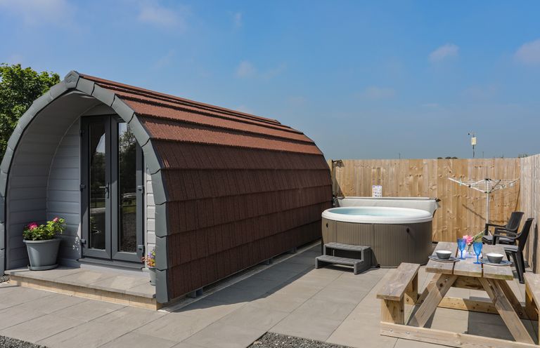 An outdoor area with a small pod structure a hot tub a wooden picnic table and chairs at Parys Pod in Amlwch