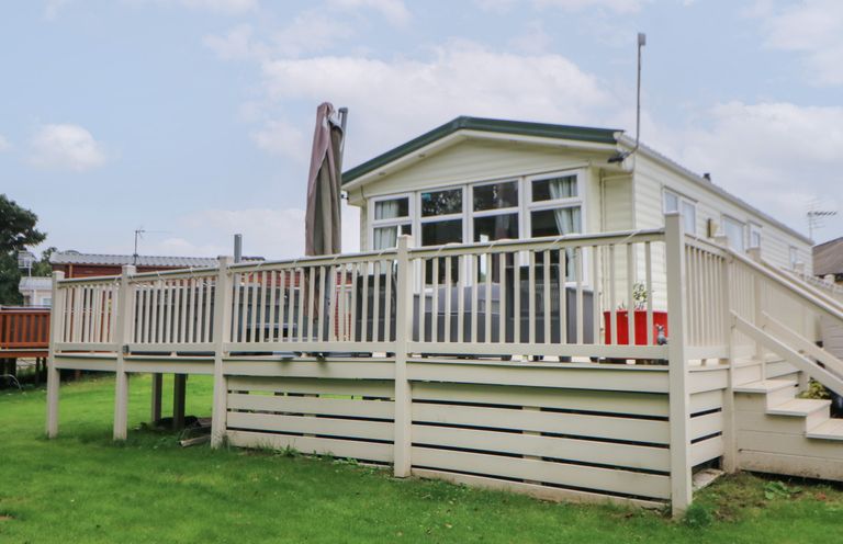 A raised deck with a railing and stairs attached to a small white house with multiple windows on a grassy lawn at Hedgehog Retreat in Felton