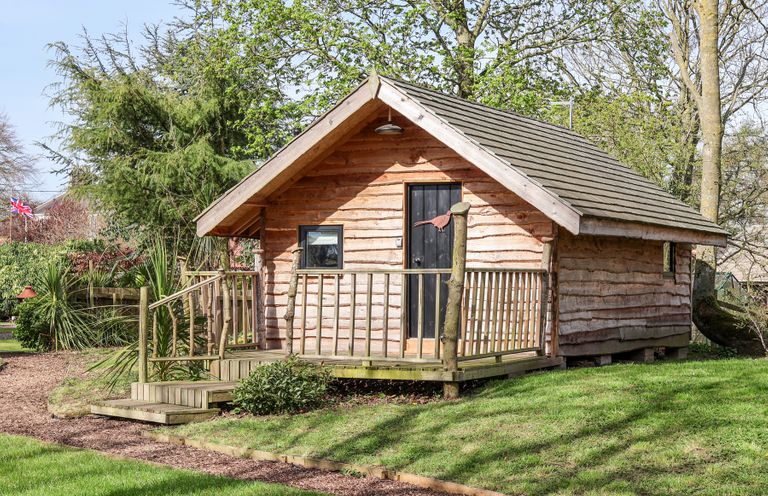 A wooden cabin with a small porch and steps surrounded by grass and trees at Pheasant in Bedale