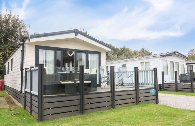 A mobile home with outdoor seating area and glass doors on a grassy plot at 3 Yealands in Carnforth