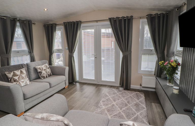 A living room with sofas pillows curtains a rug flowers on a table and a television at 24 Sherwood in Carnforth