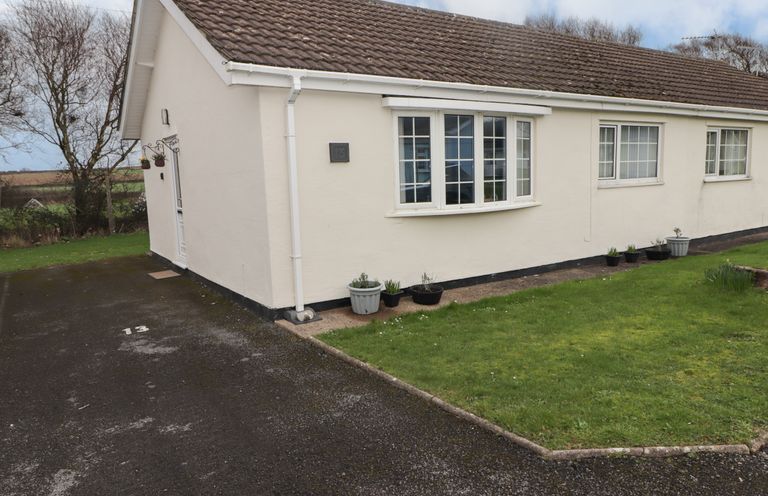 A single-story house with white walls and a tiled roof with a driveway and green lawn at 13 Gower Holiday Village in Scurlage