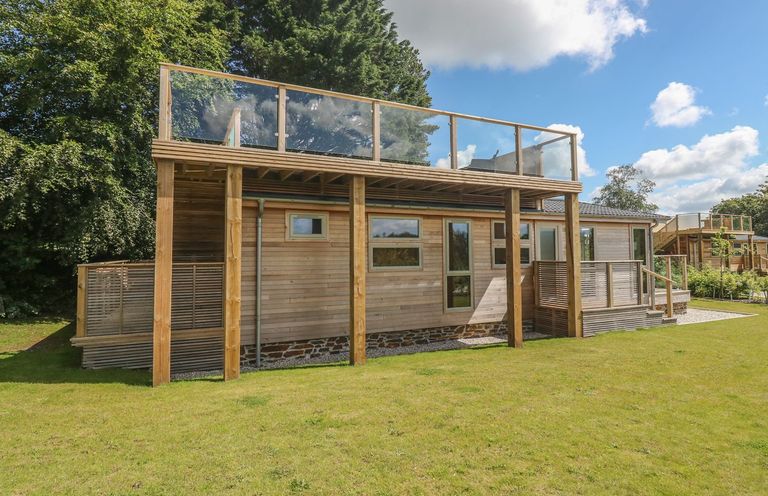 An exterior view of a wooden house with large grass lawn and balcony with glass railing at 2 Southern Place in Dobwalls