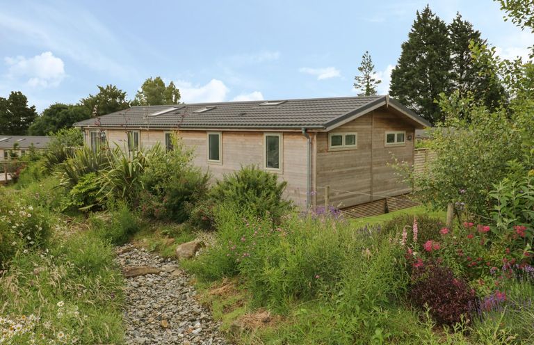 A wooden house with multiple windows surrounded by plants and a rocky pathway at 7 Faraway Fields in Dobwalls